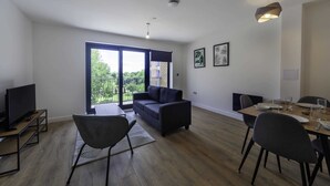 Ein modernes Wohnzimmer mit einer Couch, einem Esstisch für vier Personen und einem Fernseher auf einem Schrank.