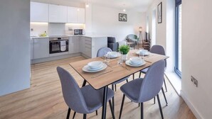 A modern kitchen with white cabinets, a dining table set with plates, glasses, and cutlery, and a grey upholstered chair.
