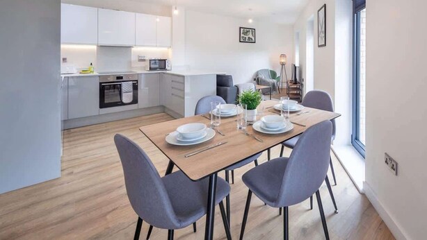 A modern kitchen with white cabinets, a dining table set with plates, glasses, and cutlery, and a grey upholstered chair.