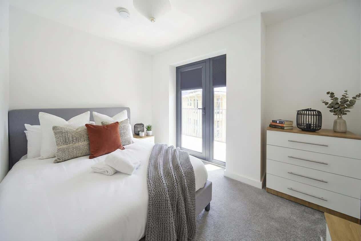 Ein Schlafzimmer mit Bett, Kommode, Fenster und Tür.