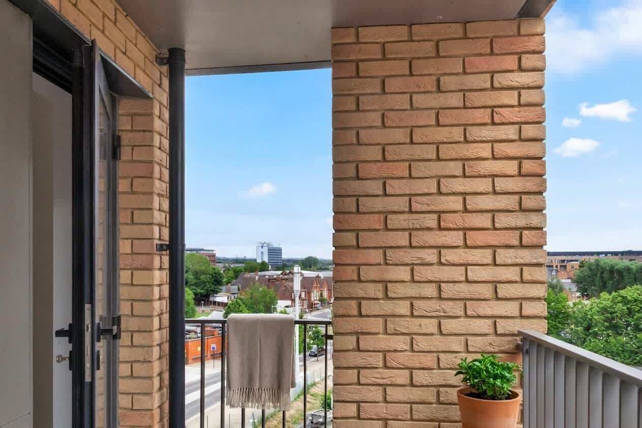 Ein Balkon mit einer Backsteinmauer, einem Blumentopf und Blick auf eine Stadtlandschaft.