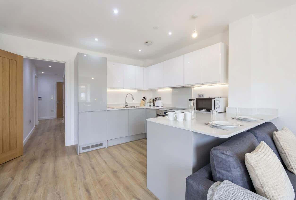 A modern kitchen with white cabinetry, a central island with seating, and a dining area with a table set for two.