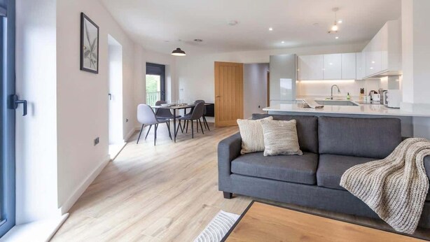 A modern living room with a grey sofa, a wooden coffee table, and a dining area with chairs.