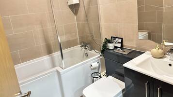 A modern bathroom with beige tiles, a bathtub, a toilet, a sink, and a shower.