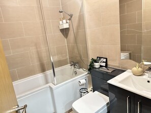 Une salle de bain avec des carreaux de couleur beige, une baignoire, des toilettes, un lavabo et une douche.