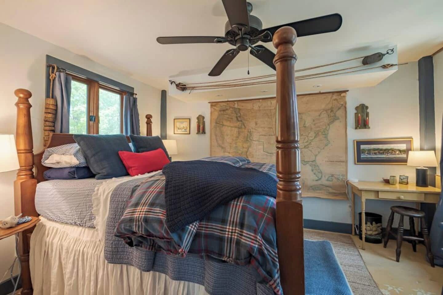 A bedroom with a four-poster bed, a desk, and a map on the wall.