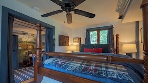 A bedroom with a wooden bed, a ceiling fan, a window with curtains, and a lamp on a bedside table.