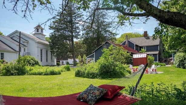 A hammock in a lush garden with a house in the background.