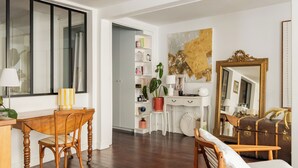 Ein Zimmer mit einem Holzesstisch, einem weißen Schreibtisch, einem großen Spiegel und einem Bücherregal.