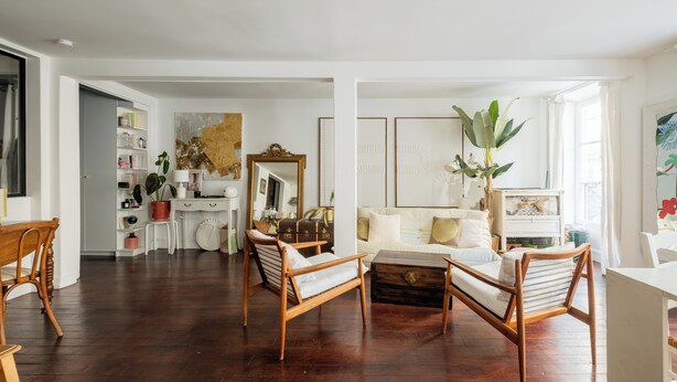 Ein geräumiges Wohnzimmer mit Holzboden, einem weißen Sofa und einem Couchtisch aus Holz. Es gibt eine Essecke mit Tisch und Stühlen, ebenfalls in Weiß.