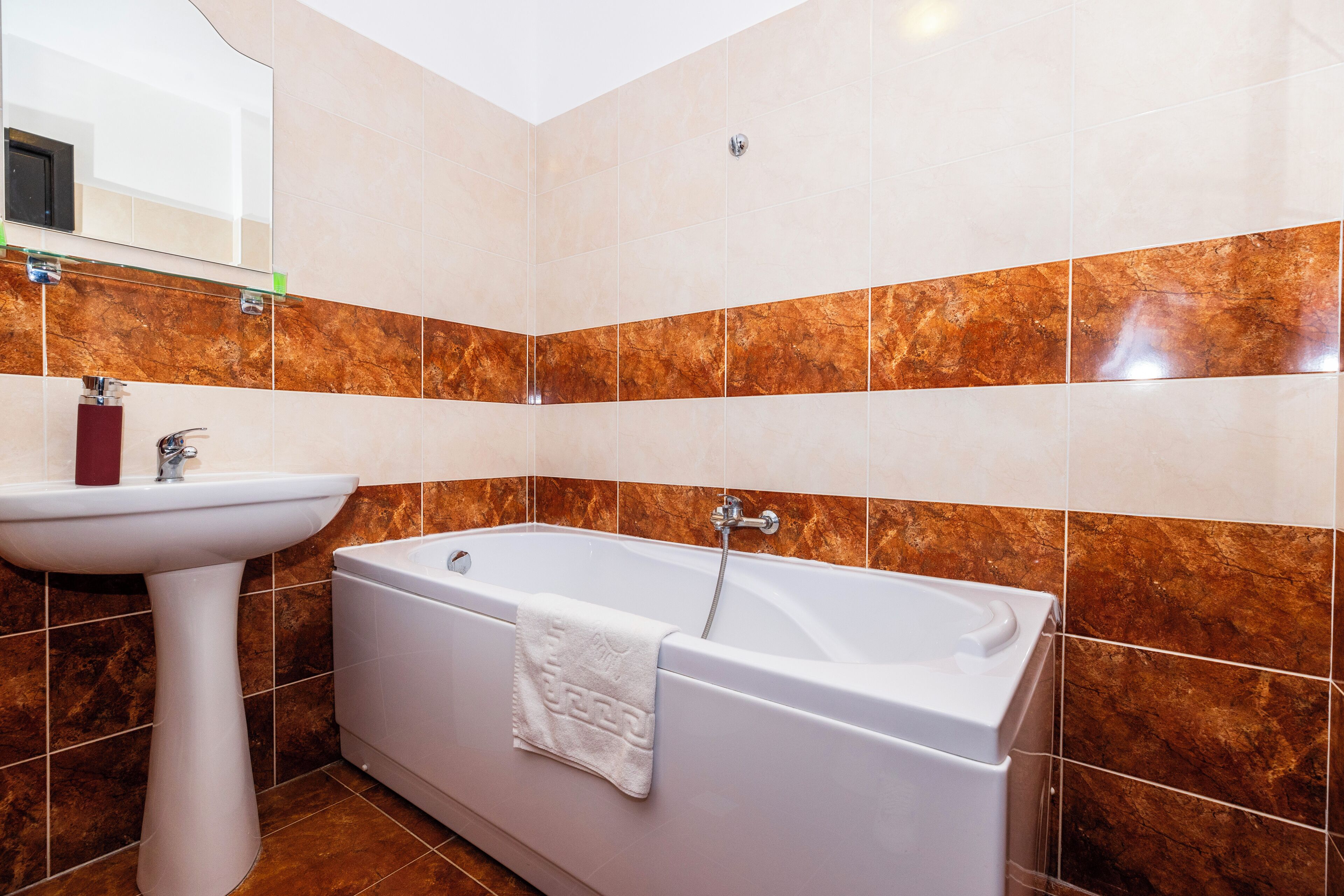 A bathroom with a white sink, a bathtub, and brown marble tiles.