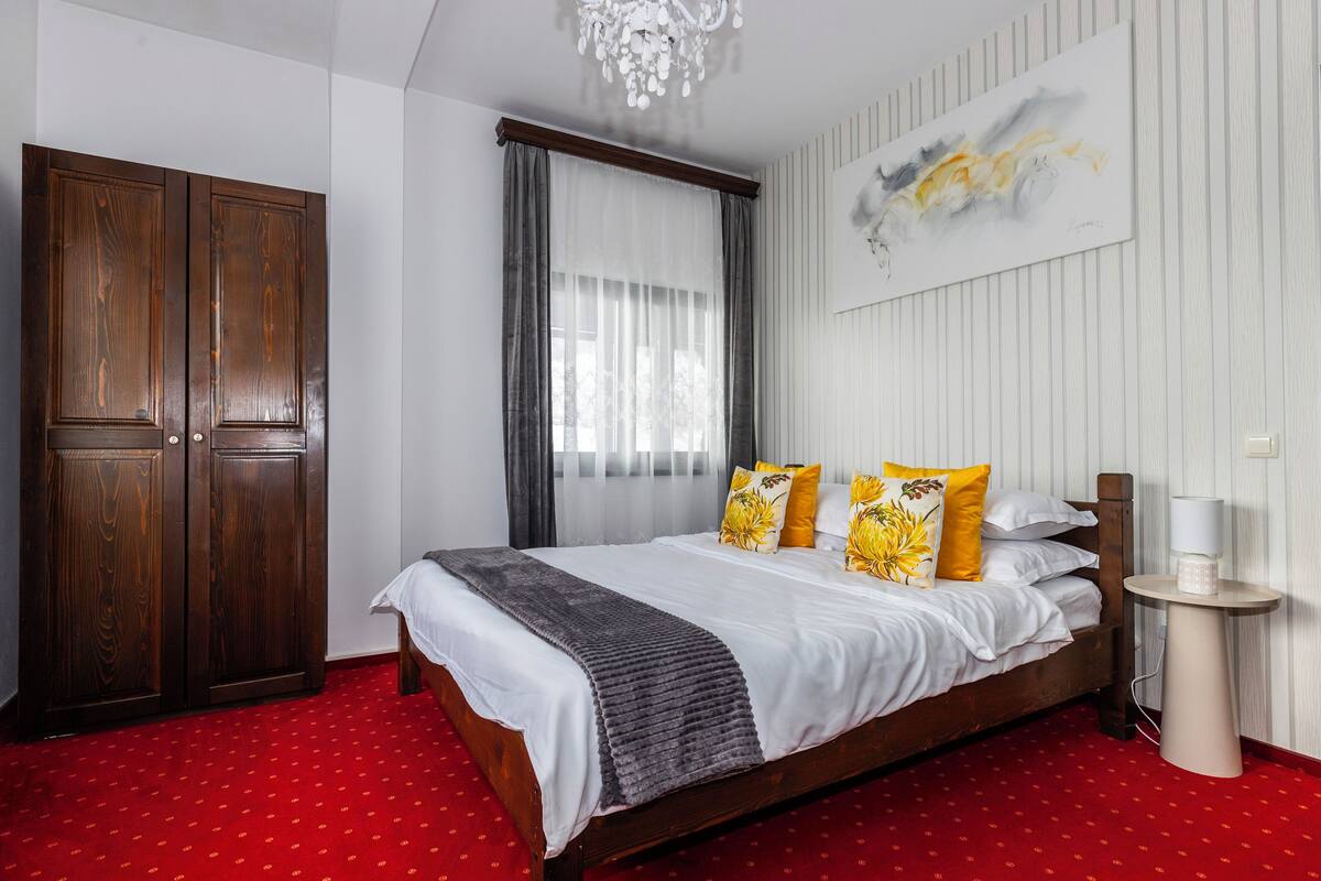 A bedroom with a wooden bed, red carpet, white walls, a chandelier, and a painting.