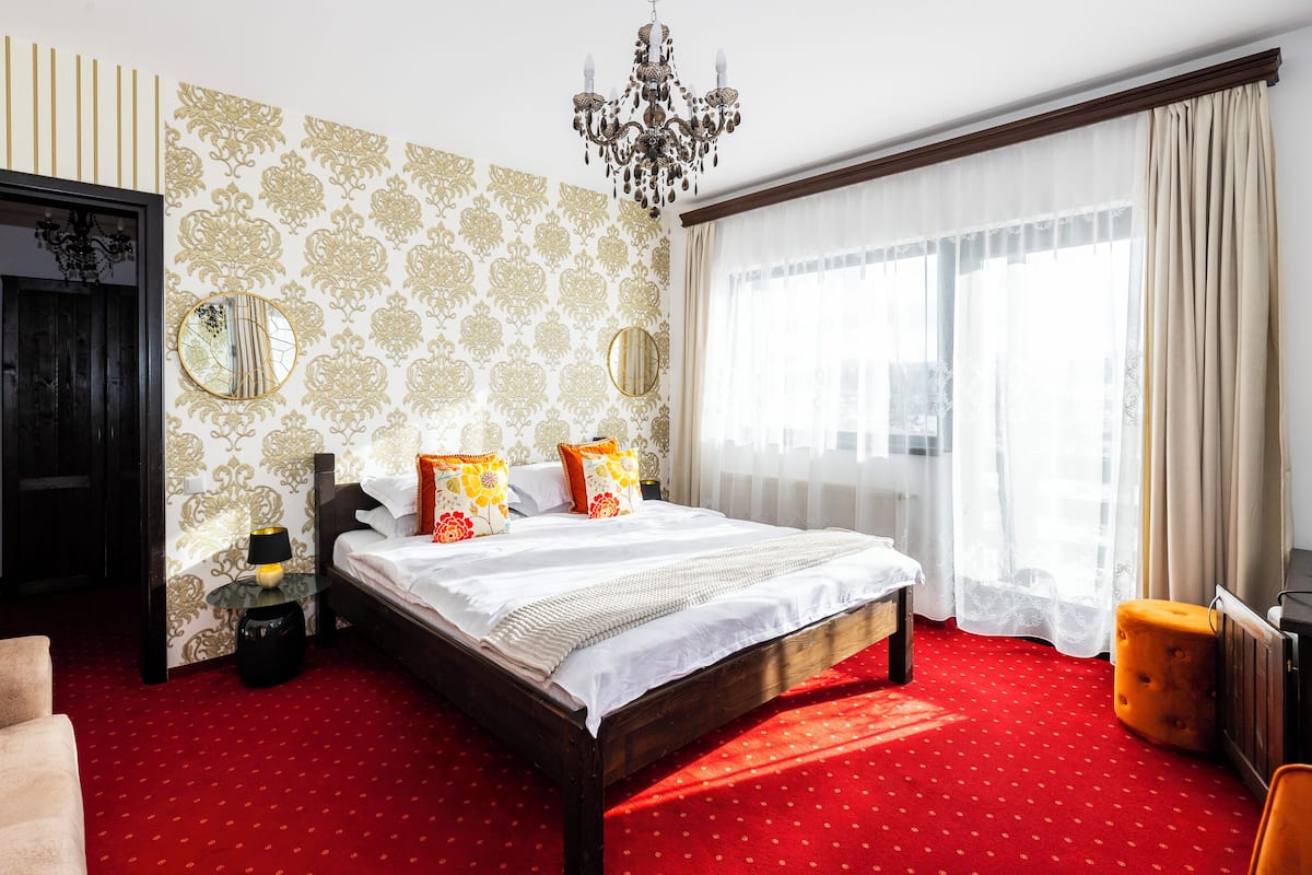 A hotel room with a large bed, two bedside tables, a mirror, a chandelier, and a window with curtains.