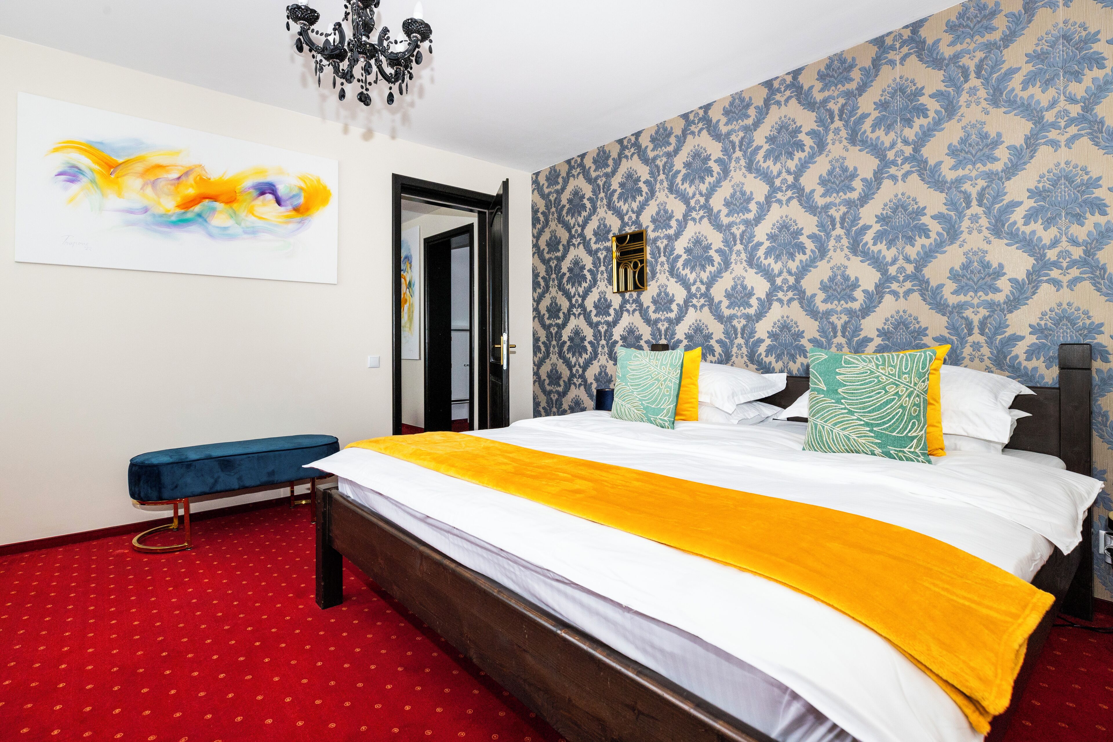 Habitación de hotel con una cama grande, un banco, una araña y papel tapiz estampado.