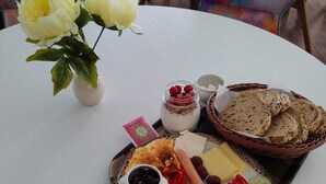 A round table with a white tablecloth, a plate of assorted foods, a vase with white flowers, and colorful chairs in the background.