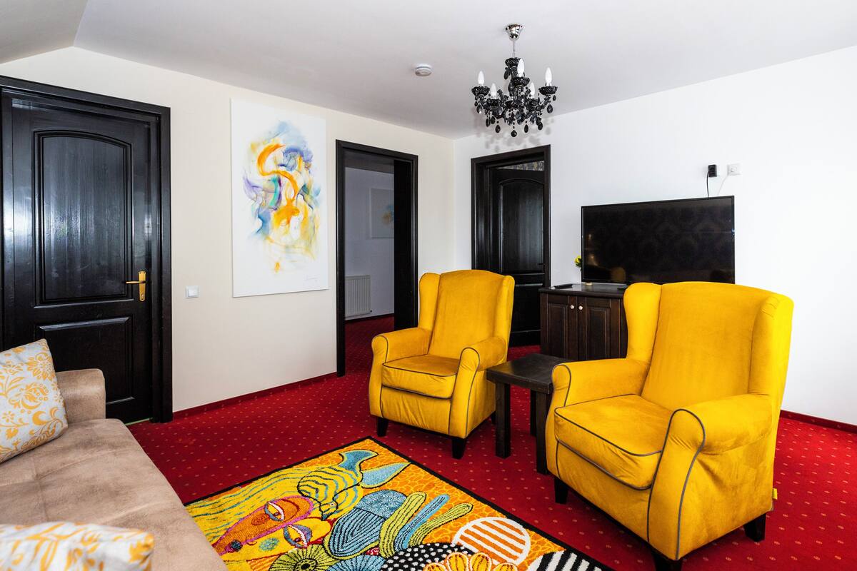 A living room with two yellow armchairs, a sofa, a red carpet, and a flat-screen TV.