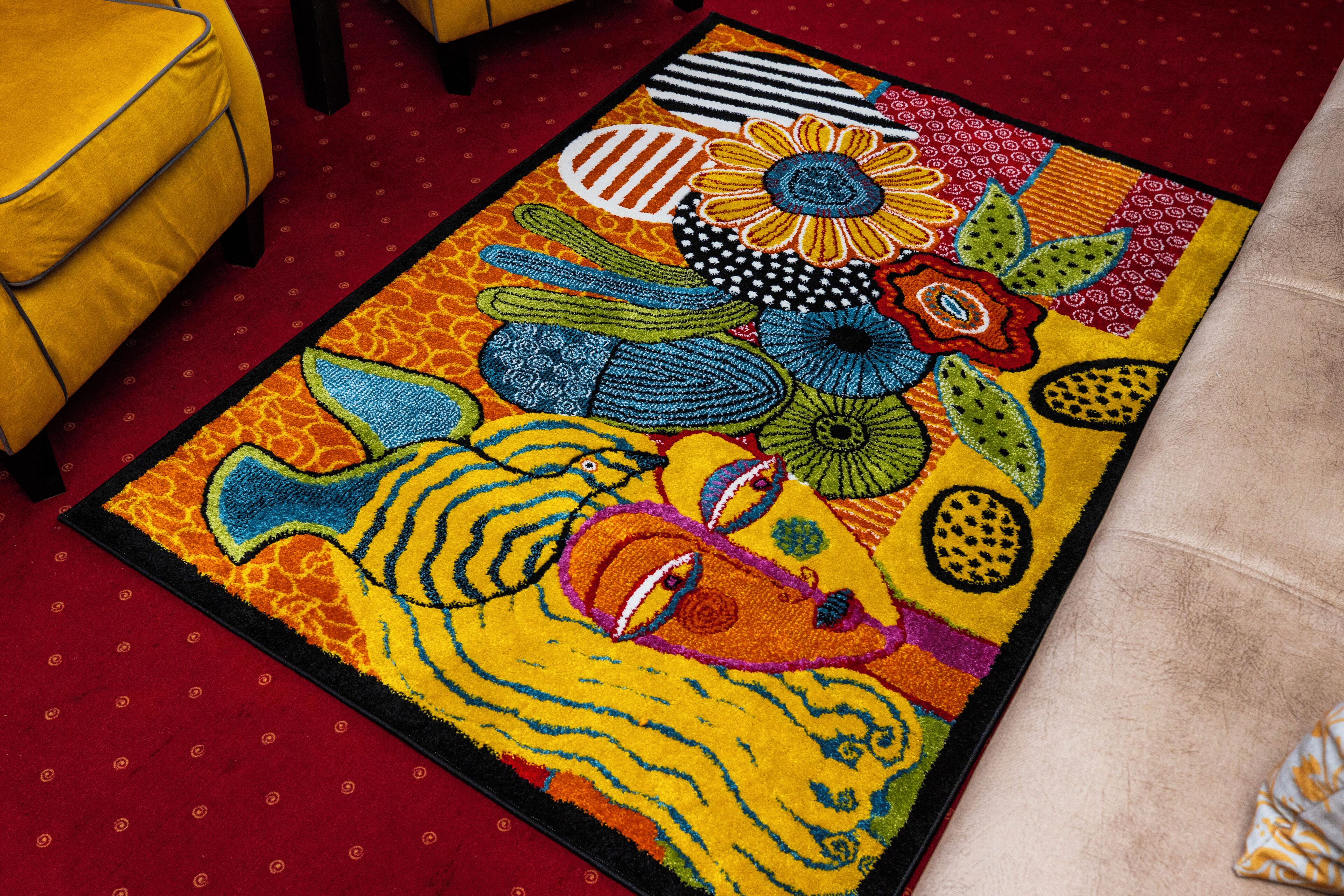 A colorful area rug with a tiger design, placed on a red carpet in a room with yellow furniture.