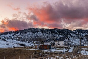 A two-story house with a balcony, surrounded by snow-covered hills and a sunset sky. - Vila Luca (Fundata)
