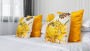 A bed with white bedding and three pillows, two with a yellow floral pattern and one solid yellow.