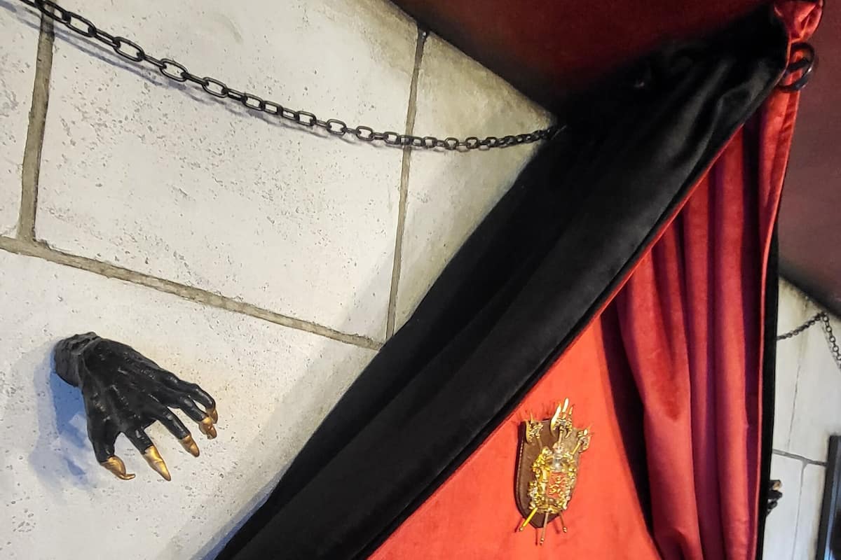 A bed with a wooden headboard, a red and black drape, and a decorative emblem on the wall.