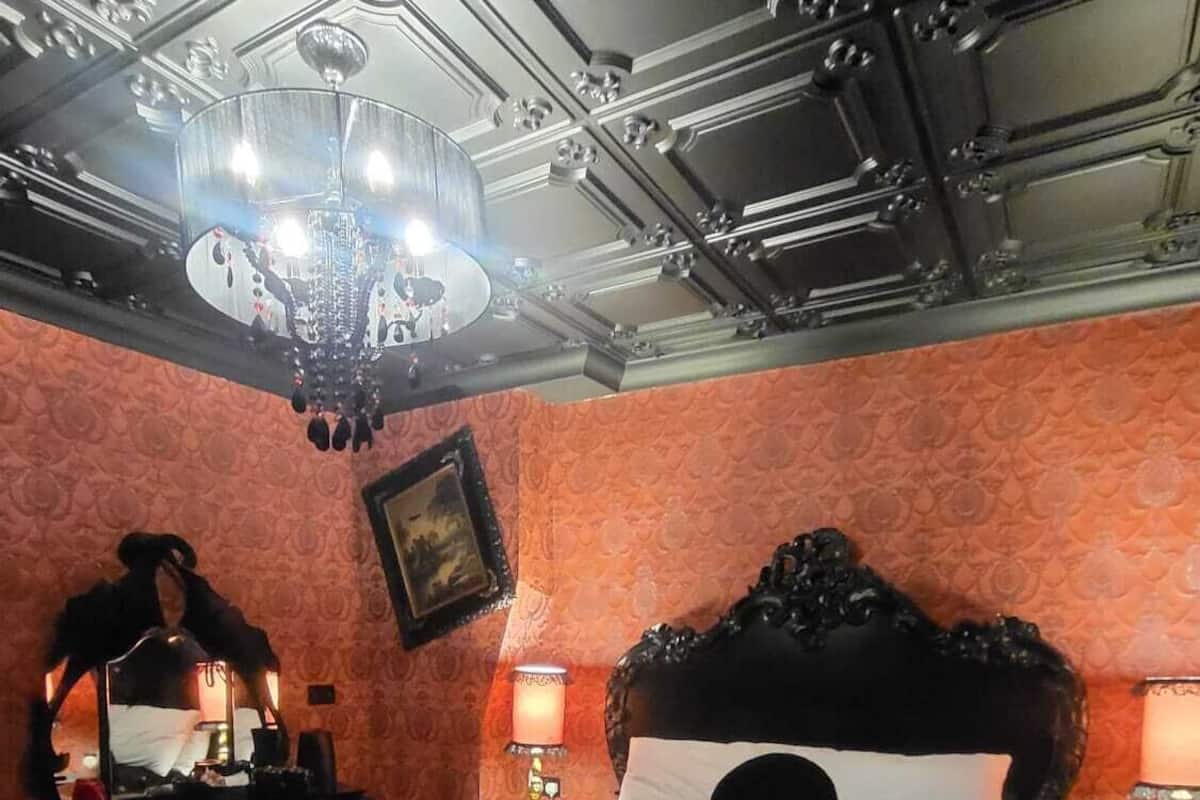 A dimly lit room with a large bed, ornate ceiling, and a chandelier.