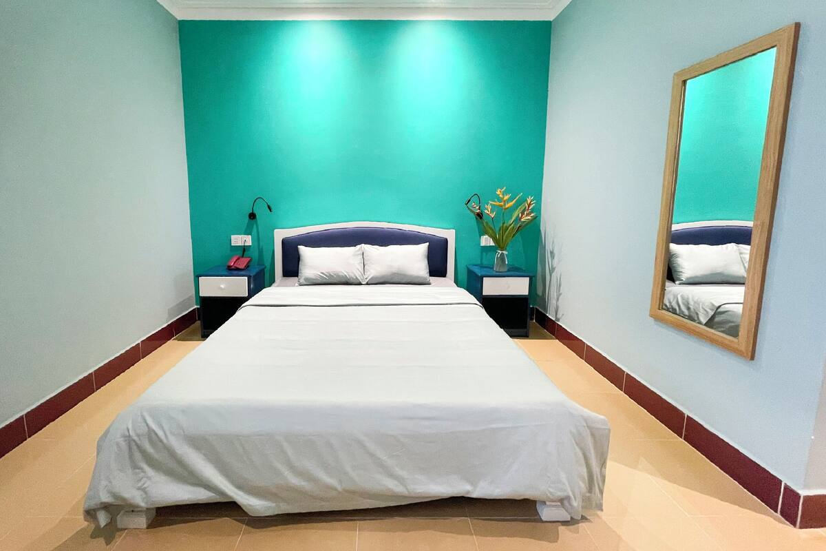 Habitación de hotel con una cama grande, dos mesitas de noche, un tocador, un espejo y una lámpara en el techo.