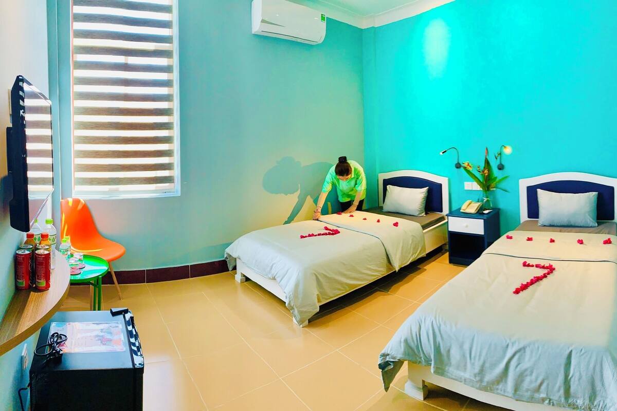 Habitación de hotel con dos camas, un escritorio con silla, televisión y ventana con persianas.
