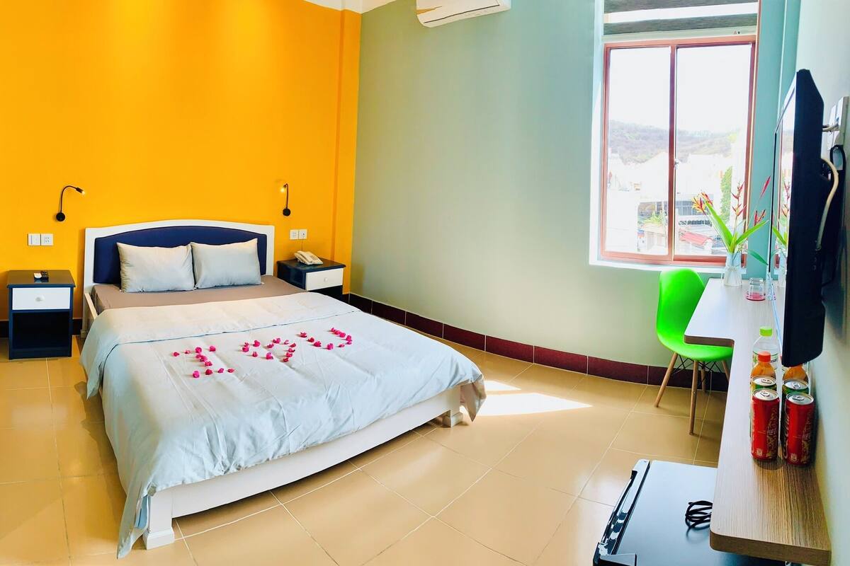 Habitación de hotel con cama, mesita de noche, silla y ventana con vistas.