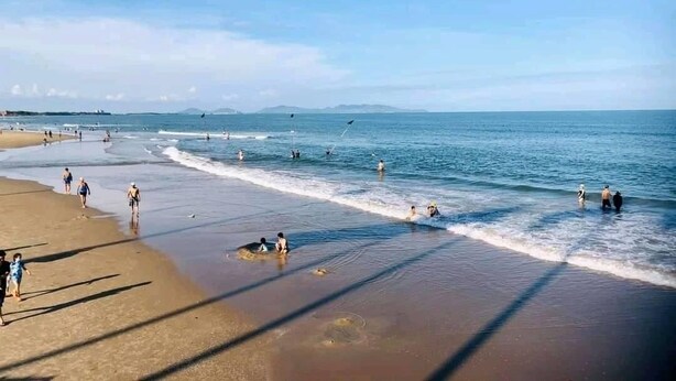 A beach with people walking and swimming, and a clear sky.