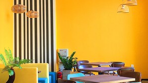 A dining area with striped walls, yellow and blue seating, and hanging wicker lamps.