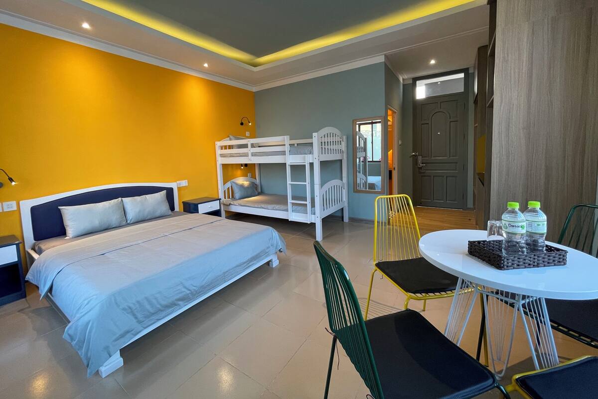 Habitación de hotel con literas, una cama individual, una mesa de comedor con sillas y una pequeña cocina.