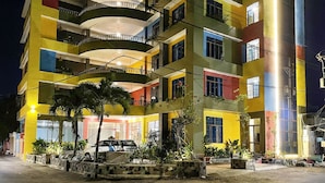 A multi-story building with balconies, a car parked in front, and potted plants.