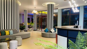A modern lobby with striped columns, a reception desk, and a seating area with sofas and ottomans.