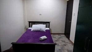 A small, simple room with a bed, a door, and a patterned floor. - Cozy, Safe, and Secure Two-Bedroom Apartment Unit (San Carlos City)