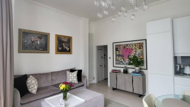 A modern living room with a grey sofa, a coffee table, a glass dining table, and a kitchen area visible through an open door. - Modern 2 bed Apartment in Notting Hill (London)