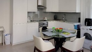 A modern kitchen with white cabinets, a round dining table with chairs, and a hanging light fixture. - Modern 2 bed Apartment in Notting Hill (London)