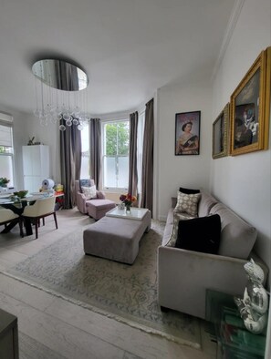 A modern living room with a sofa, ottoman, and a dining area with a table and chairs.