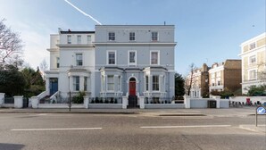 A two-story building with a red door and white trim, located at a street corner. - Modern 2 bed Apartment in Notting Hill (London)