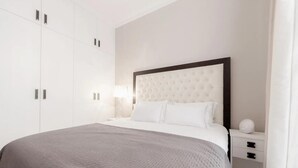 A bedroom with a large bed, a nightstand, a wardrobe, and a wall-mounted lamp. - Modern 2 bed Apartment in Notting Hill (London)