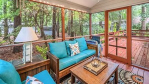 Un espace extérieur accueillant, aménagé avec un banc en bois, un canapé confortable et une table, le tout entouré de grandes fenêtres donnant sur une zone boisée.
