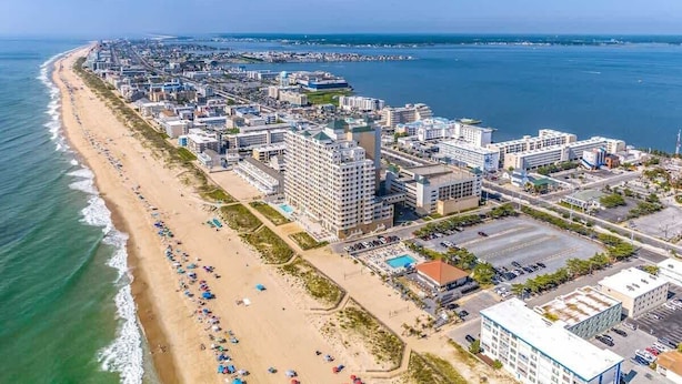 Vue aérienne d’une ville côtière avec une longue plage, un grand complexe hôtelier et un port de plaisance.