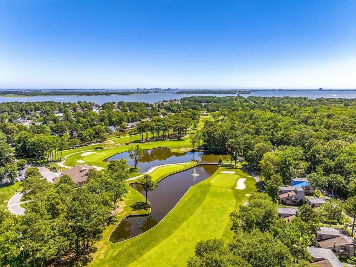 A golf course with a pond, surrounded by trees and residential buildings.