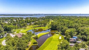 A golf course with a pond, surrounded by trees and residential buildings.