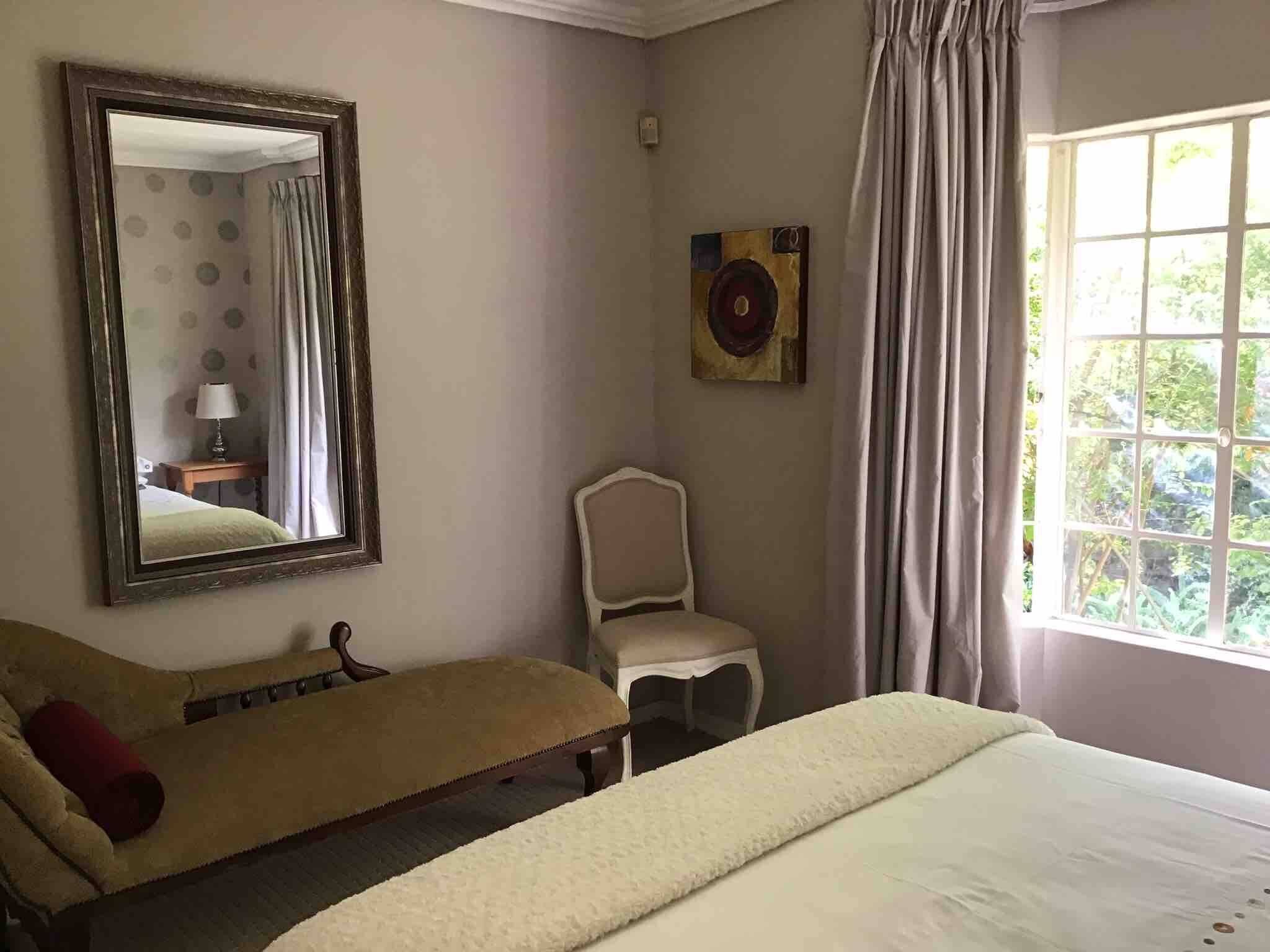 Un dormitorio con cama, una silla, un espejo y una ventana con cortinas.