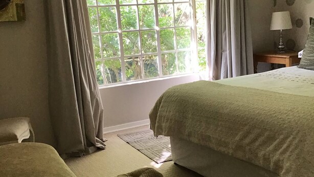Une chambre avec une grande fenêtre, un lit, une table de chevet avec une lampe et une chaise.