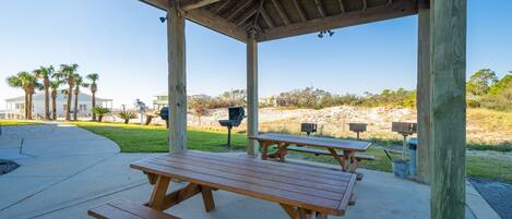 Et overdækket picnicområde med træbænke og borde, grill og skraldespande.