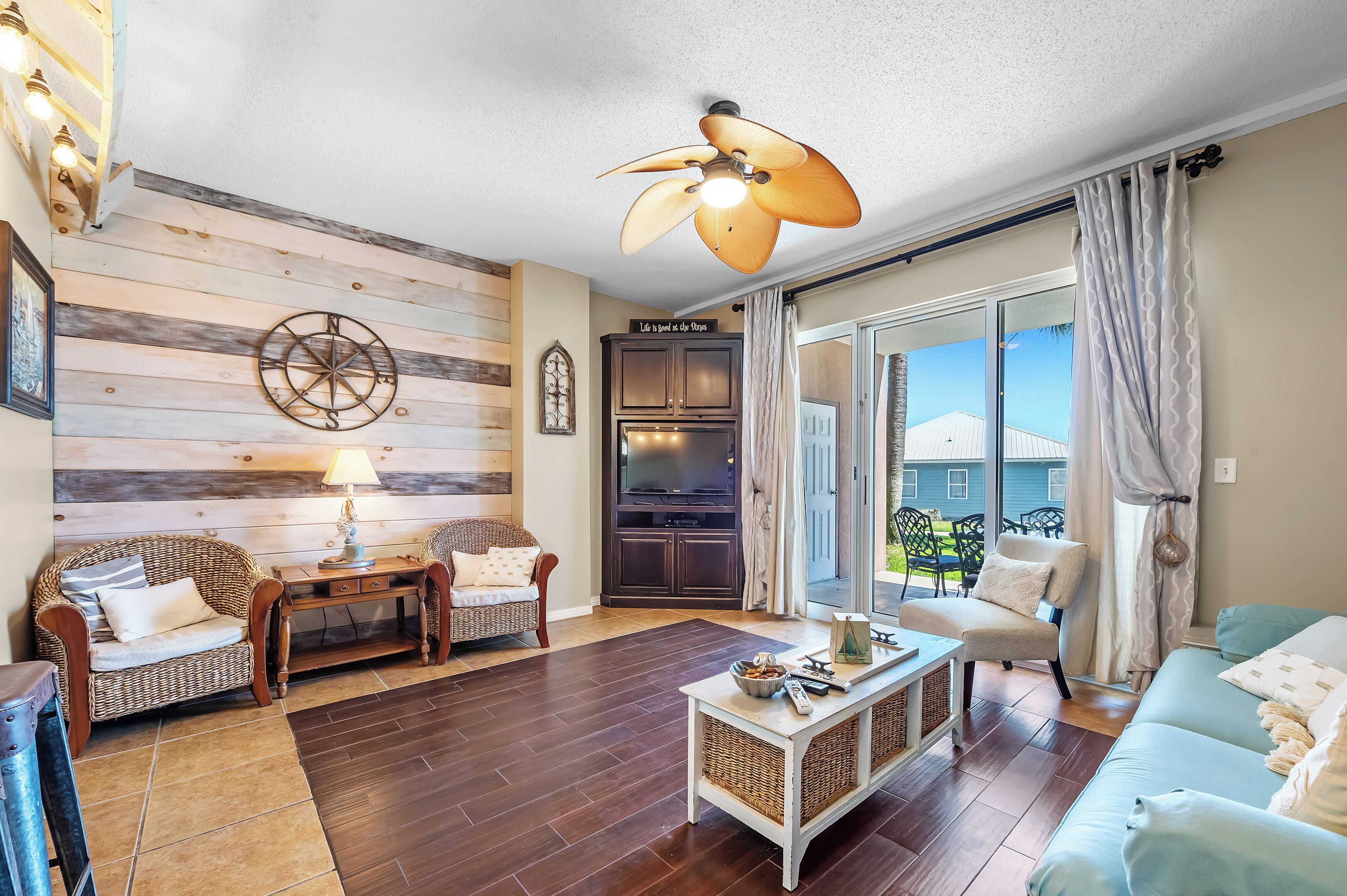 Un salon confortable avec un ventilateur de plafond, un téléviseur et une vue sur l’extérieur.