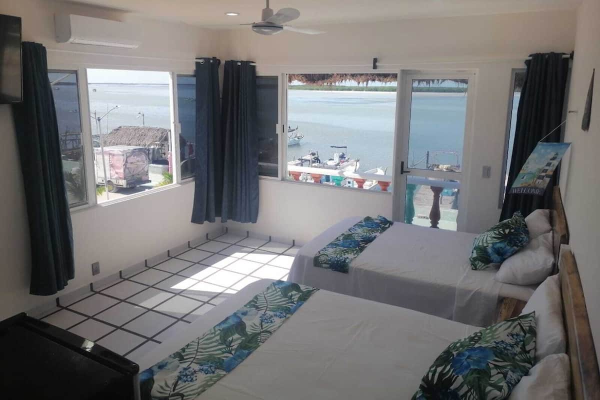 Une chambre d’hôtel avec deux lits, un ventilateur de plafond et vue sur la mer.