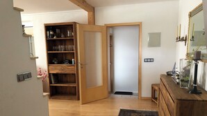Una habitación con piso de madera, una puerta grande abierta que da a otra habitación, un mueble de madera pequeño y un espejo en la pared.