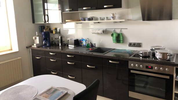 Una cocina moderna con armarios negros, electrodomésticos de acero inoxidable y encimera blanca.